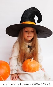 Halloween Portrait Of A Little Girl In A Witch Magic Hat. Little Child With Pumpkins. White Background. 