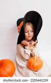 Halloween Portrait Of A Little Girl In A Witch Magic Hat. Little Child With Pumpkins. White Background. 