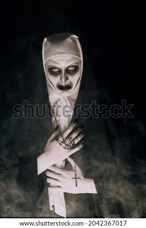 Halloween. Portrait of a scary devilish nun with bloody eyes looking at camera on a black background. Horrors.