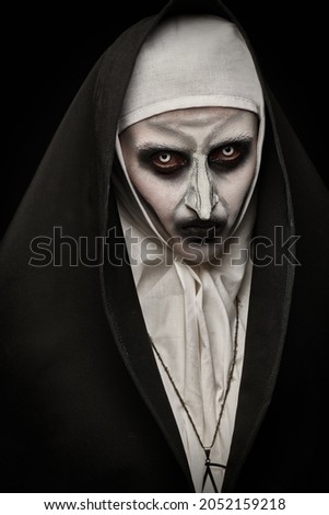 Halloween. Portrait of a scary devilish nun with bloody eyes looking at camera on a black background. Horrors.