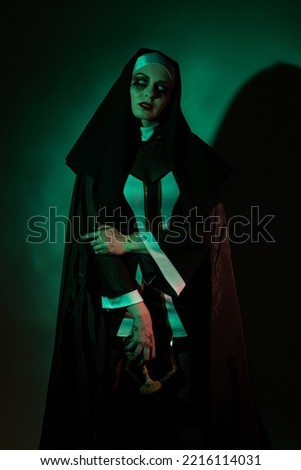 Halloween. Portrait of a scary devilish nun eyes looking at camera on a black and green background.