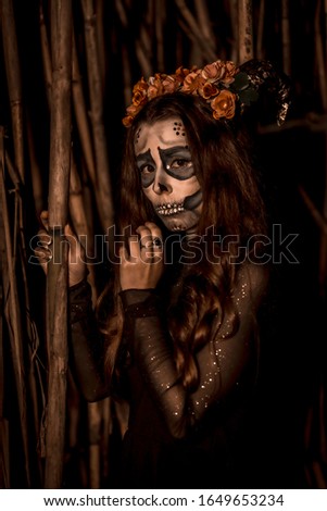 Halloween, portrait of a young woman dressed as a Mexican skull grabbing a bamboo, with yellow lighting