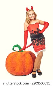 Halloween. Pretty blonde girl child in an imp costume poses with a large pumpkin on a white background. Studio portrait.  - Shutterstock ID 2203503831