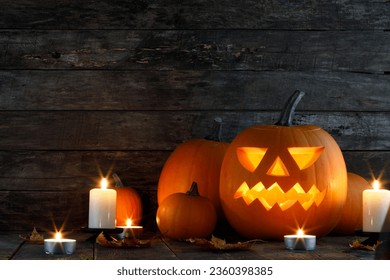 Halloween pumpkin glowing jack o lantern with carved face and candles on wooden background, banner with copy space for text