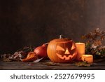 Halloween pumpkin head jack lantern with dried-up leaves. Halloween holidays art design, celebration. Carved Halloween pumpkin with burning candle.
