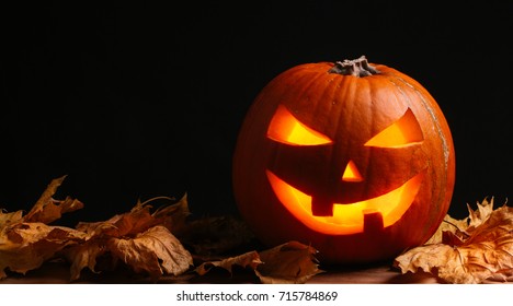 Halloween pumpkin lantern with dry leaves with black background