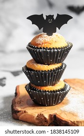 Halloween Pumpkin Muffins In Black Capsules Decorated With Cardboard Bats. Festive Halloween Cupcakes. Close-up View Of Delicious Spooky Halloween Muffins On The Grey Background. Halloween Recipes