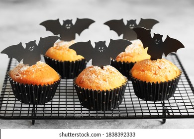 Halloween Pumpkin Muffins In Black Capsules Decorated With Cardboard Bats. Festive Halloween Cupcakes. Close-up View Of Delicious Spooky Halloween Muffins On The Grey Background. Halloween Recipes