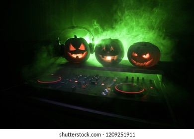 Halloween pumpkin on a dj table with headphones on dark background with copy space. Happy Halloween festival decorations and music concept. Empty space. Selective focus