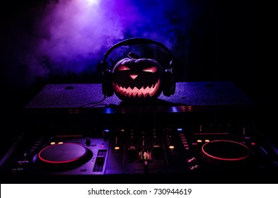 Halloween pumpkin on a dj table with headphones on dark background with copy space. Happy Halloween festival decorations and music concept