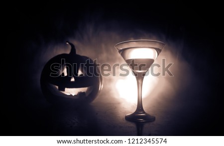 Halloween pumpkin orange cocktails. Festive drink. Halloween party. Funny Pumpkin with a glowing cocktail glass on a dark toned foggy background. Selective focus