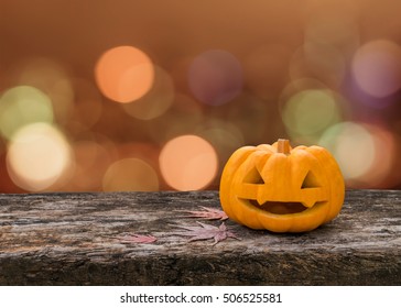 Halloween pumpkin orange Jack O'Lantern happy smiling face on grunge wood table with red autumn leaves, candle light lit bokeh for halloween party holiday celebration decoration