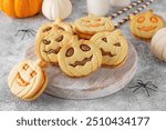 Halloween pumpkin shaped sandwich cookies with sweet cream filling on a wooden board with milk on a concrete background. Jack o lantern cookies