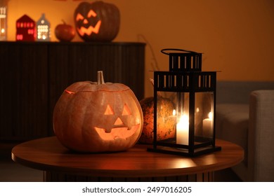 Halloween pumpkins with burning candle on table in dark living room - Powered by Shutterstock