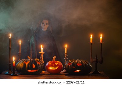 Halloween Pumpkins With Burning Candles And Death In  Mantle On Dark Background