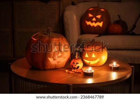 Halloween pumpkins with candies and burning candles on table in dark living room