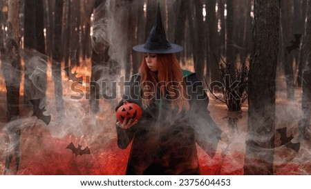 Halloween, red-haired Witch with a pumpkin in a dark forest. A girl in the smoke performs witchcraft.