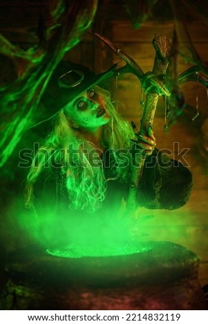 Halloween scary tales. An old, ugly and scary witch brews a witch's potion in her lair. Witch is illuminated with magical green light.
