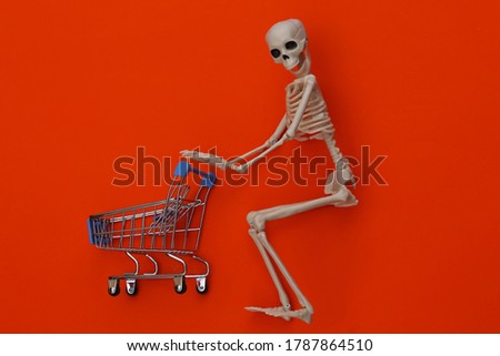 Halloween, scary theme. Skeleton and shopping trolley on orange background.