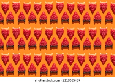 Halloween seamless pattern jelly beans in the shape of devil head on an orange background with hard shadow. Festive sweets pattern, candy gummy trick or treat. Splash screen and wrapping paper mockup