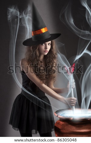 halloween shot of a young and beautiful witch wearing a huge black and orange hat making a poison in a big pot