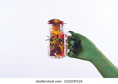 Halloween Spooky Green Witch Hand Holding Jar Of Colorful Candies With Little Black Spiders On White Background