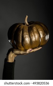 Halloween Symbol Of Painted Gold Pumpkin Vegetable Metallized Color In Female Golden Hand On Grey Background