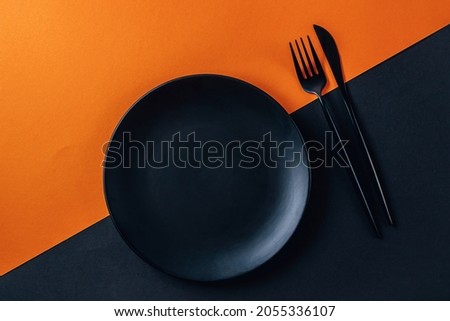 Halloween table setting with an empty black plate and cutlery a black and orange background.