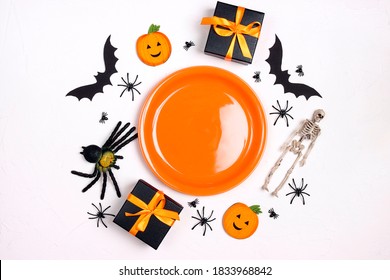 Halloween Table Setting With Orange Plate, Spooky Decorations And Gifts On White Table. Top Down Composition.