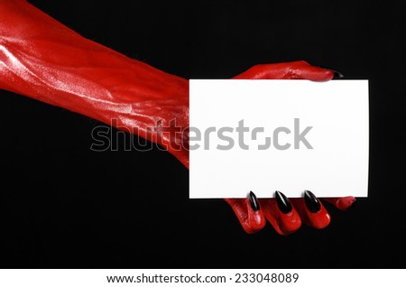 Halloween theme: Red devil hand with black nails holding a blank white card on a black background
