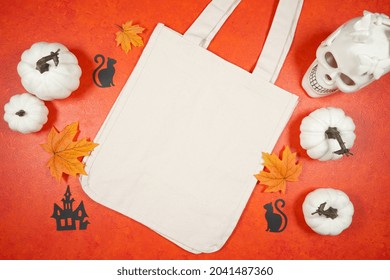 Halloween Theme Trick Or Treat Canvas Tote Bag Mockup With White Skull Pumpkins On A Bright Textured Orange Background. Product Mock Up With Negative Copy Space.