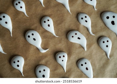 It’s Halloween time! A festive scene featuring spooky ghost-shaped meringues resting on parchment paper. The season of cookies with playful and creepy faces has arrived, bringing the eerie spirit. - Powered by Shutterstock