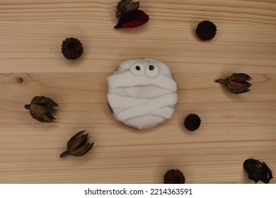 A Halloween White Ghost Spooky Cookie With Dark Chocolate Decorations On Top Of A Light Wood Board. There Are Dry Brown Autumn Leaves Decorating The Background.  Wallpaper Of A Party Celebration.