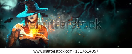 Halloween Witch girl with magic Book of spells portrait. Beautiful young woman in witches hat conjuring, making witchcraft. Over spooky dark magic forest background. Wide Halloween party art design