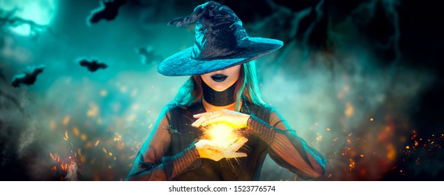 万圣节女巫女孩正在制作巫术，手里拿着魔法，咒语。漂亮的年轻女子在巫婆的帽子魔术。幽灵般的黑暗魔法森林背景。魔术师。宽版万圣节派对艺术设计