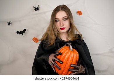 Halloween Witch Holding A Pumpkin Against Background With Spiderweb,bats Etc