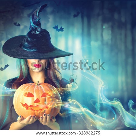 Halloween Witch with a magic Pumpkin in a dark forest. Beautiful young woman in witches hat and costume holding carved pumpkin. Halloween art design