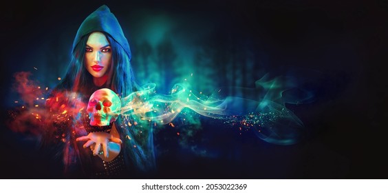 Halloween Hexe, die eine menschliche SchädelLaterne in ihren Händen hält. Schönes junges Mädchen. Dunkelheit. Gruselige Kulisse. Auf unscharfem, dunklem, magischem Hintergrund. Magisches Konzept. Kunstdesign. 
