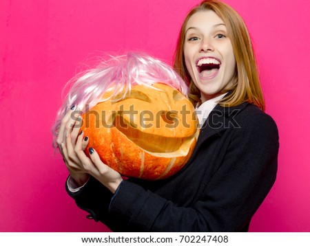 Halloween woman with happy face. Woman in coat and scarf at pink wall. Party and traditional food. Holiday and celebration. Girl with orange scary pumpkin in wig.