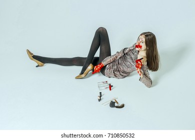Halloween Woman Lying On Floor Isolated On White. Girl With Bloody Face And Long Brunette Hair. Fashion Model In Grey Party Dress. Lady With Lipstick And Makeup Kit. Halloween Make Up Concept.