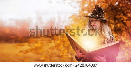Halloween a woman with a magic spell book in a witch hat is conjuring, performing witchcraft over the autumn background of the forest.