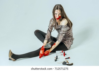 Halloween Woman Sitting On Floor Isolated On White. Girl With Bloody Face And Hands. Fashion Model In Grey Party Dress With Makeup Kit. Halloween Make Up Concept.