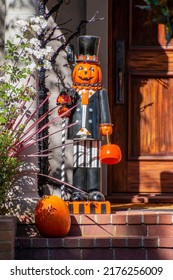 Halloween A Wooden Man Stands On A Porch. It Has A Orange Pumpkin Head, Top Hat, Black Suit, Black Shoes, Stripped Pants. He Carries A Pumpkin. A Front Door Is To His Right, A Pumpkin Is On The Porch.