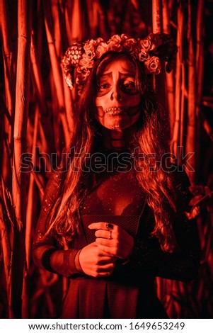 Halloween, a young woman dressed as a Mexican skull among bamboos, with red lighting