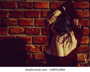 Halloween zombie girl pretty young woman with bloody brunette hair with wounds and red blood outdoors on brick wall