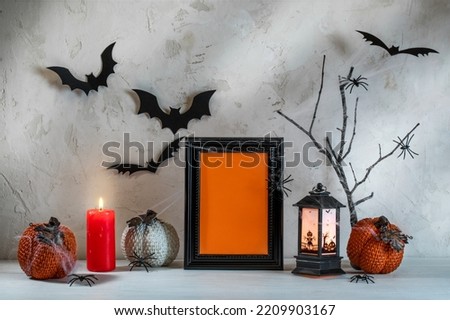 Hallowen festive composition on white wooden table on textured backdrop. Decorative pumpkins, black frame, bats, spiders, burning candle, lantern, cobwebs. Halloween decorations. Mock up. Copy space.