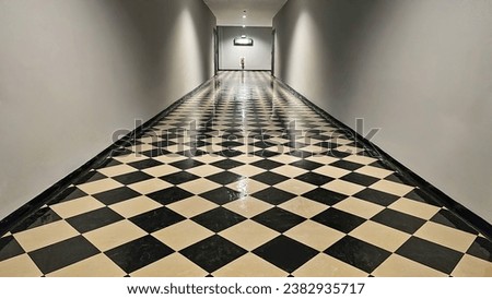 The hallway with black and white checkered tiles on the floor with fire exit sign on wall, Corridor in the building along two doors leading to fire escape. Thailand, November 1, 2023