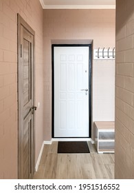 Hallway Design In A Small Apartment With Beige Walls And Brick Texture. White Front Door, Shoe Cabinet, Clothes Hanger.
