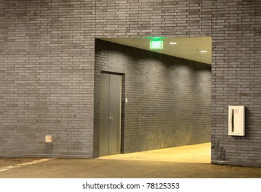 A Hallway With Grey Brick And An Exit Sign.