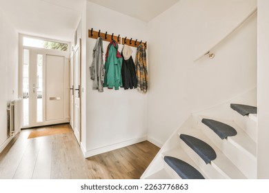 a hallway with white walls and wooden flooring there is a coat rack on the wall next to the stairs